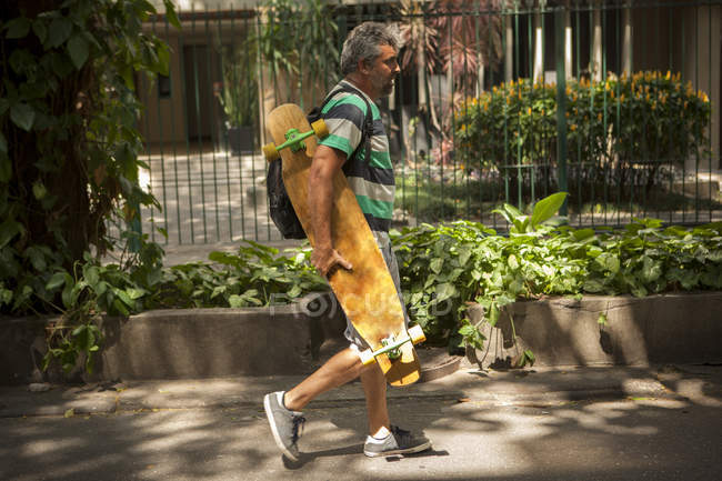 Mature man strolling on sidewalk carrying skateboard, Rio De Janeiro, Brazil — Stock Photo
