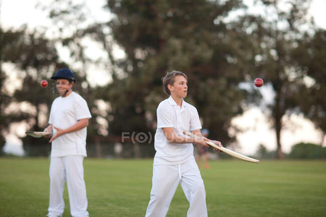 Chicos practicando golpeando pelota de cricket con bate - foto de stock