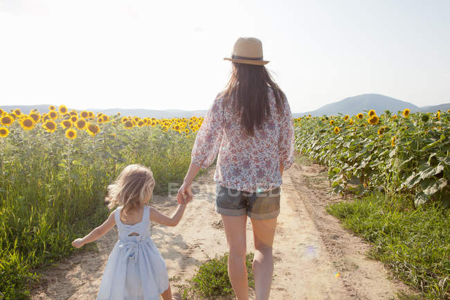 Mother and daughter walking through field of sunflowers — Stock Photo