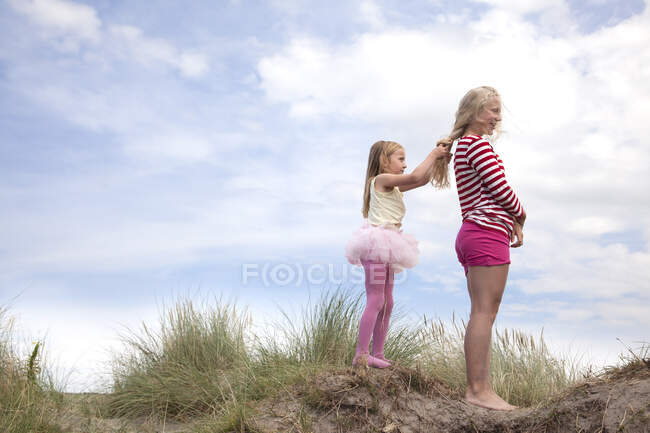 Two girls on dunes, one plaiting friend's hair, Wales, UK — Stock Photo