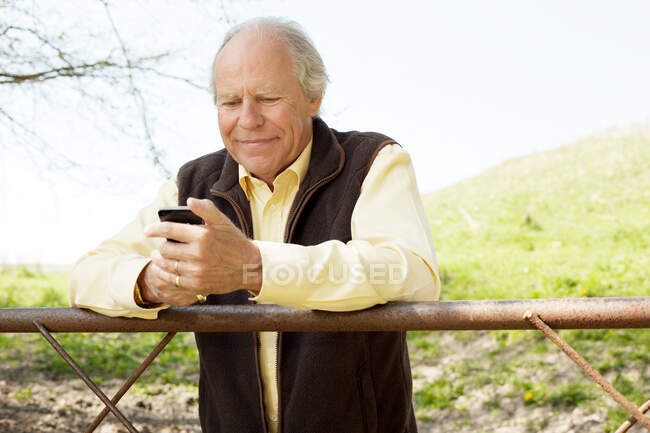 Hombre mayor sonriendo en el mensaje en el teléfono móvil - foto de stock