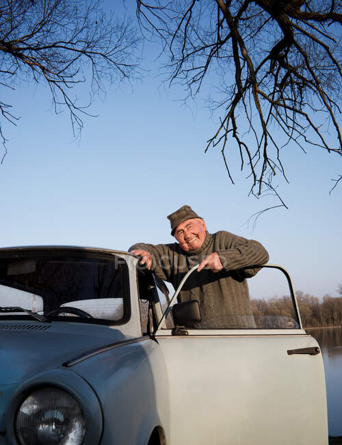 Senior man standing by car on riverside — Stock Photo