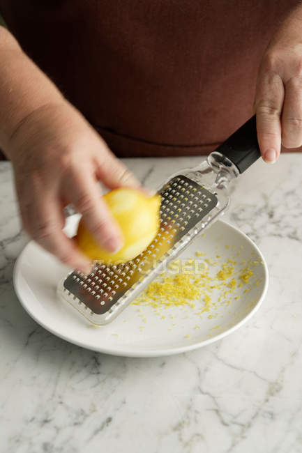 Chef grating lemon in bowl, close-up partial view — Stock Photo