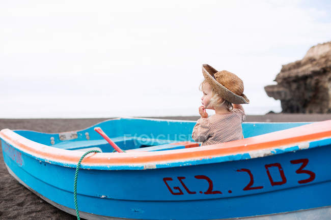 Toddler girl in straw hat sitting in rowing boat on beach — Stock Photo