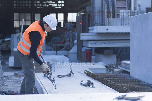 Trabajador de fábrica que fija el gancho del cabrestante al bloque de hormigón en fábrica de refuerzo de hormigón - foto de stock