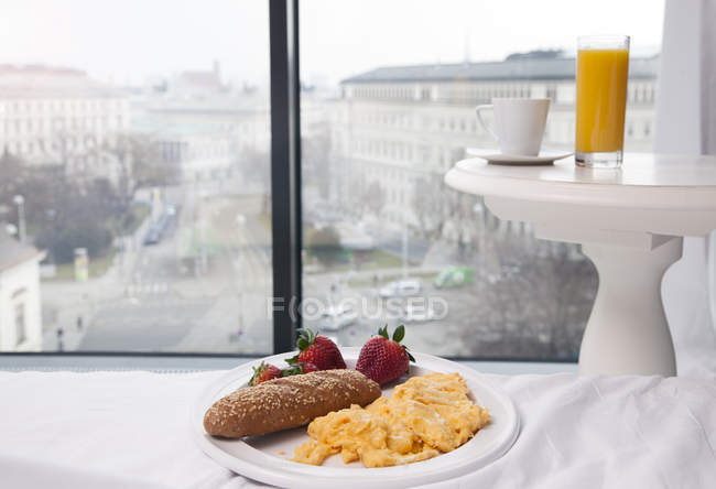 Huevos revueltos, jugo y café por ventana con vista a la ciudad - foto de stock