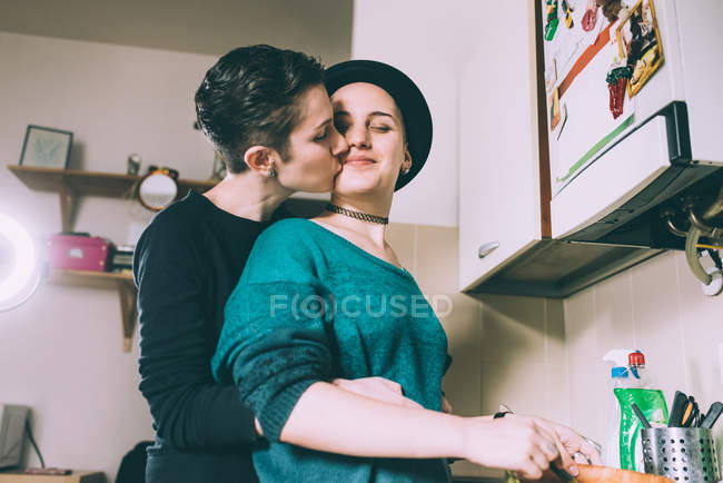 Young woman kissing girlfriend in kitchen — Stock Photo
