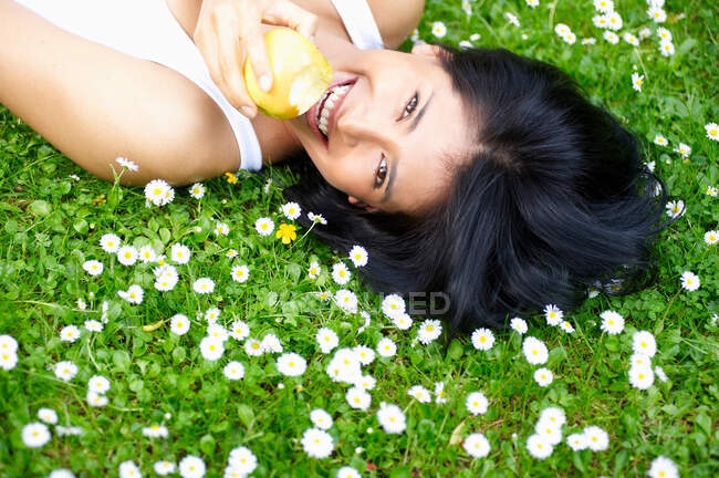 Frau isst einen Apfel im Gänseblümchen — Stockfoto