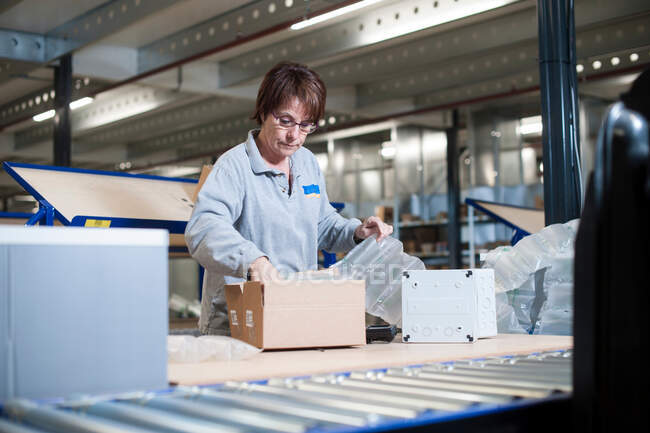 Female warehouse worker packing box for conveyor belt — Stock Photo