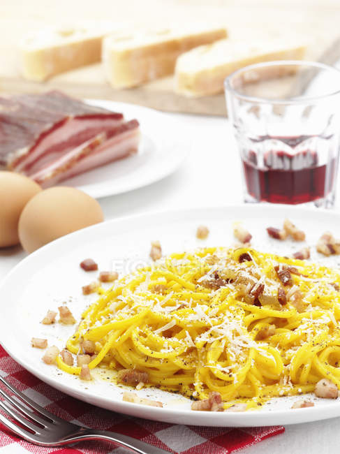 Plate of pasta carbonara with ingredients on table — Stock Photo