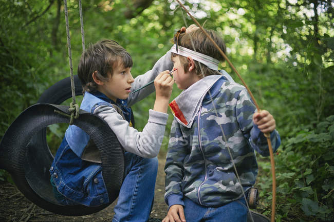 Boy face painting friend whilst playing in forest — Stock Photo