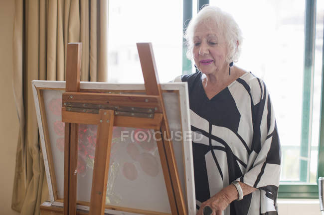 Seniorin bemalt Kunst auf Leinwand in Rentnervilla — Stockfoto
