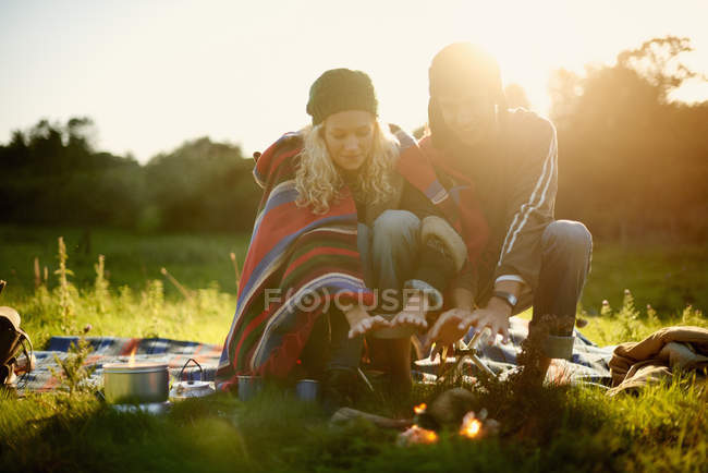 Young camping couple warming hands by campfire at dusk — Stock Photo
