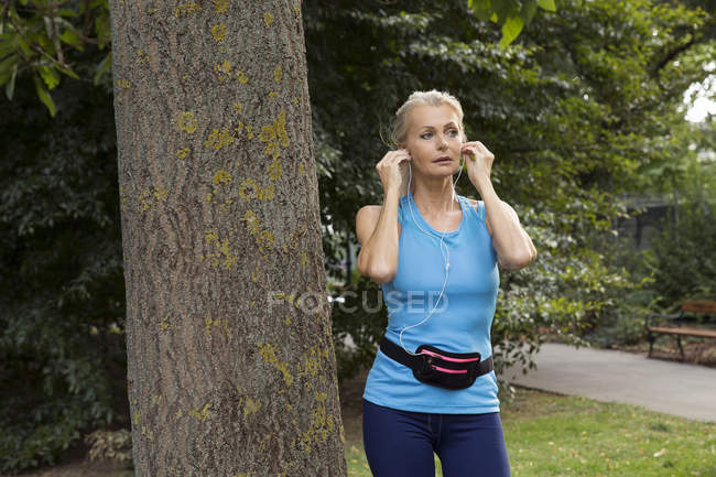 Donna matura regolazione auricolari durante l'allenamento nel parco — Foto stock