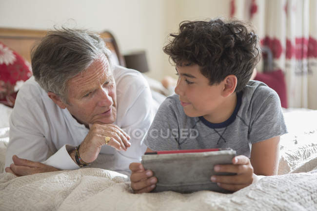 Homem e neto sênior, relaxando na cama, olhando para tablet digital — Fotografia de Stock