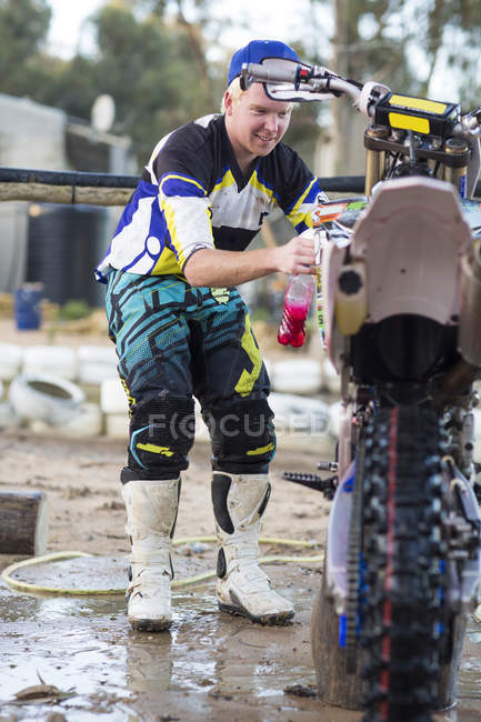 Young male motocross competitor cleaning motorcycle — Stock Photo