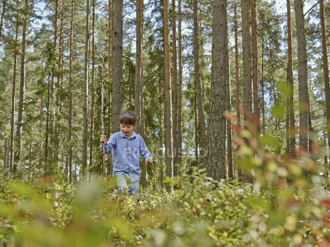 Junge läuft mit Stock durch Wald — Stockfoto