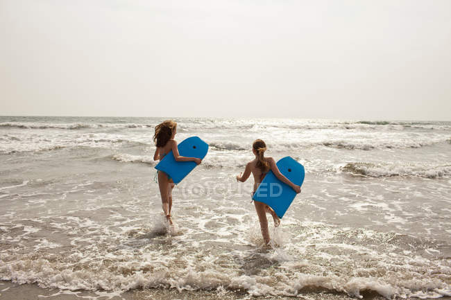 Girls carrying boogie boards in waves — Stock Photo