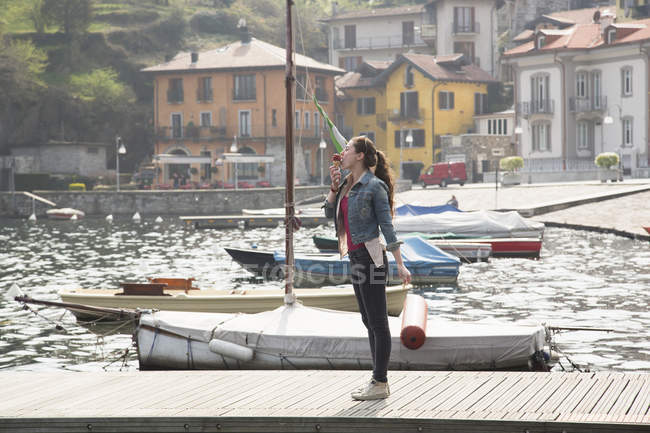 Young woman standing on pier eating ice cream cone at lake Mergozzo, Verbania, Piemonte, Italy — Stock Photo