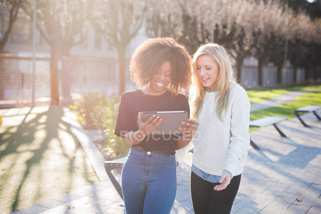 Две молодые подруги в парке, глядя на цифровую табличку, Комо, Италия — стоковое фото