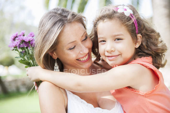 Daughter hugging mother and holding bunch of flowers — Stock Photo