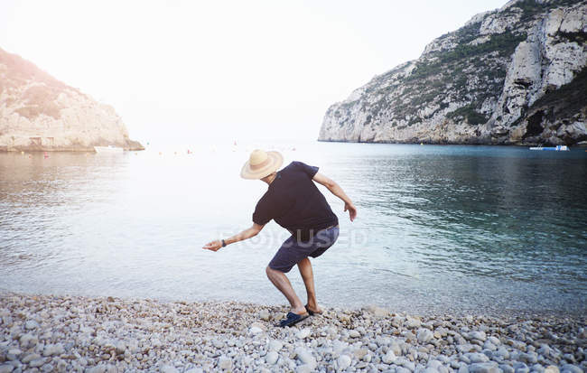 Вид сзади на молодого человека, скимминг камни с пляжа, Хавея, Испания — стоковое фото