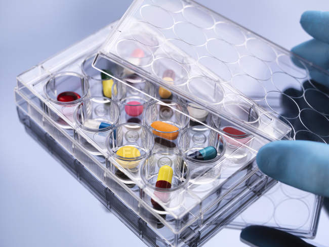 Hand removing lid from variety of medical drugs, pharmaceutical research — Stock Photo