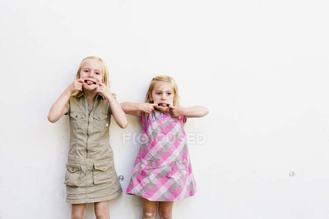 Portrait de deux jolies sœurs tirant des visages devant un mur blanc — Photo de stock