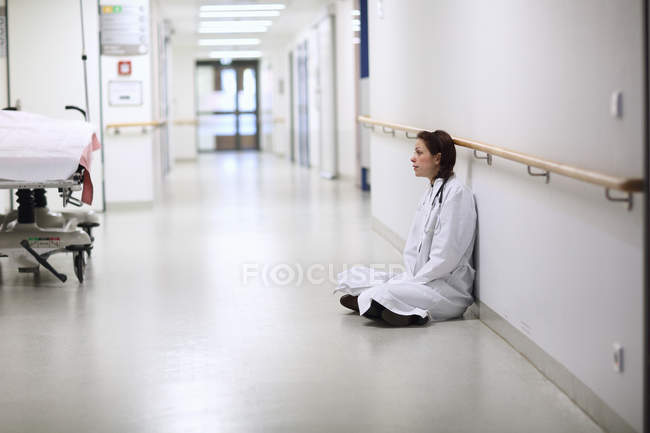 Doctora sentada con las piernas cruzadas en el pasillo del hospital - foto de stock