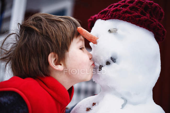 Ragazzo baciare pupazzo di neve, fuoco selettivo — Foto stock