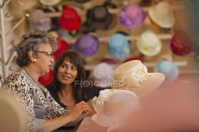 Milliner decorating hat for customer in shop — Stock Photo