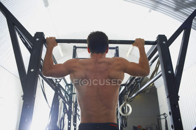 Мужчина делает подтяжки в спортзале, вид сзади — стоковое фото