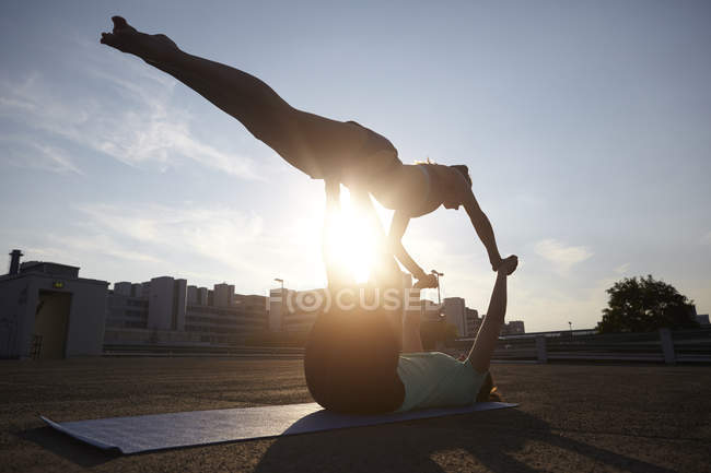 Two silhouetted young women practicing yoga in urban parking lot — Stock Photo