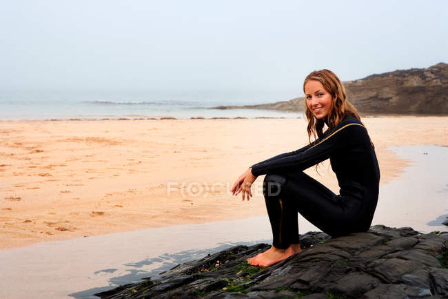 Frau sitzt im Neoprenanzug am Strand — Stockfoto