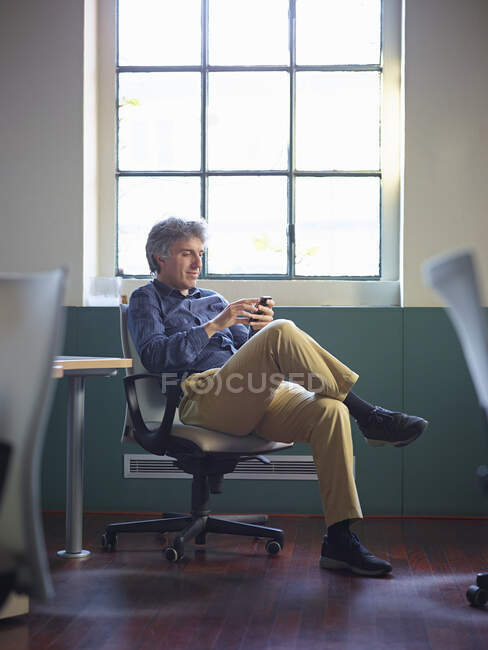 Зрілий бізнесмен сидить на офісному стільці з мобільним телефоном — стокове фото
