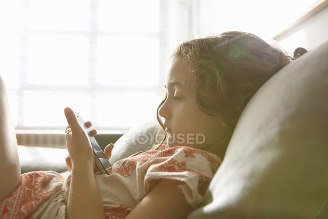 Девушка лежит на диване в гостиной, просматривает смартфон — стоковое фото