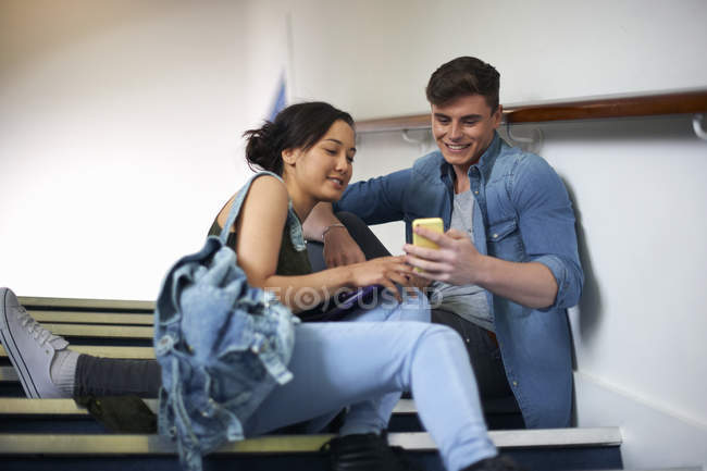 Jeune couple d'étudiants lisant des textes de smartphone sur escalier — Photo de stock