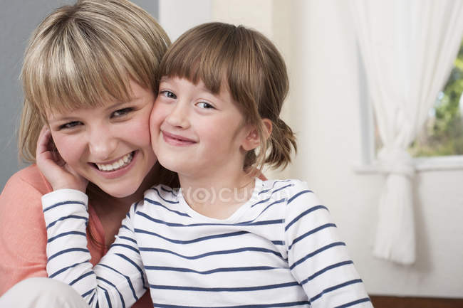 Portrait of young woman and pre-adolescent girl smiling and looking in camera — Stock Photo