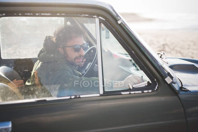 Man in parked vintage car lat beach fastening window — Stock Photo