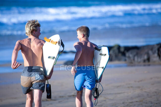 Dos surfistas adolescentes corriendo hacia el mar, Fuerteventura, España - foto de stock