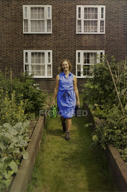 Young woman carrying watering can on council estate allotment — Stock Photo