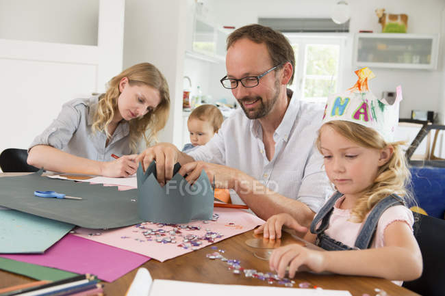 Familie mit zwei Töchtern stellt Papierkronen her — Stockfoto
