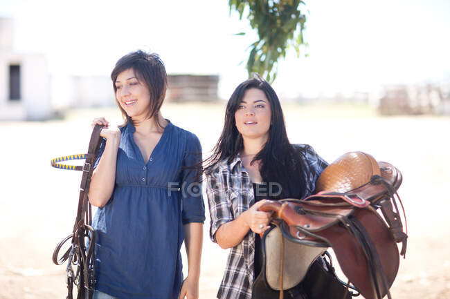 Jovens mulheres carregando sela e corda — Fotografia de Stock