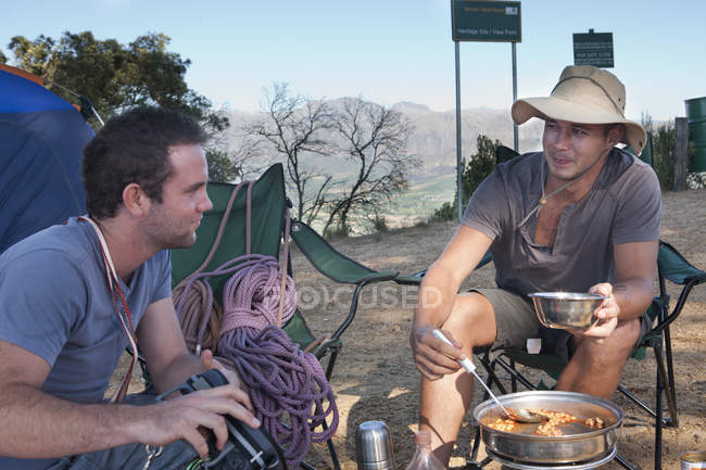 Двоє молодих чоловіків таборів спілкуються і готують їжу — стокове фото