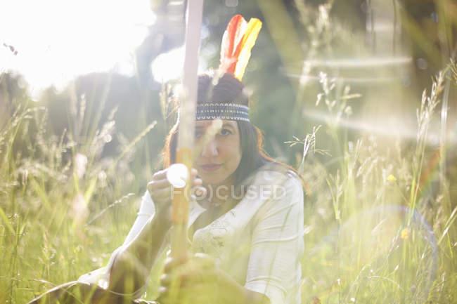 Портрет зрілої жінки в довгій траві, що тримає лук і стрілу — стокове фото
