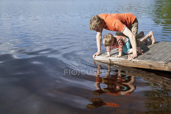 Отец и сын смотрят в озерную воду с пирса, Сомерниеми, Финляндия — стоковое фото
