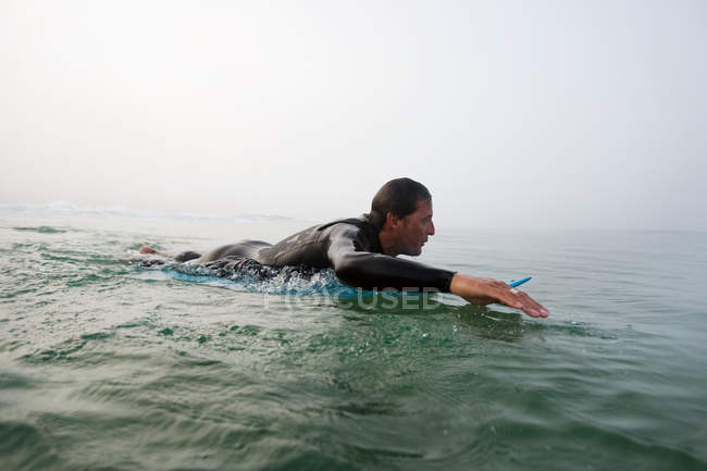 Uomo sdraiato su tavola da surf nell'acqua dell'oceano — Foto stock