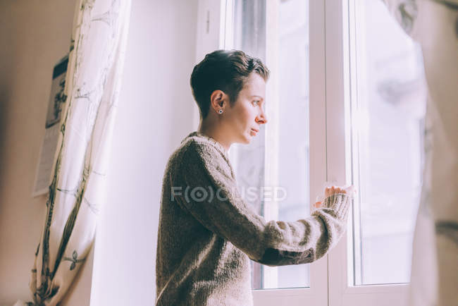 Portrait of young woman staring through window at home — Stock Photo