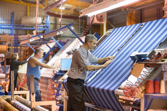 Trabajadores textiles inspeccionando hilos tejidos a rayas en molino - foto de stock