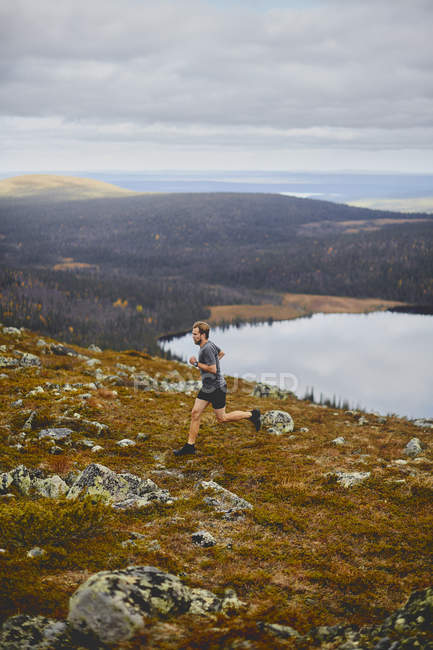 Man trail running on rocky cliff top, Keimiotunturi, Lapland, Finland — Stock Photo
